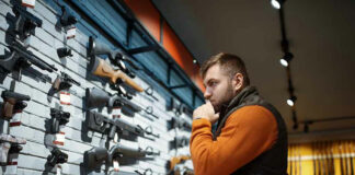 Man contemplating firearms displayed on wall.
