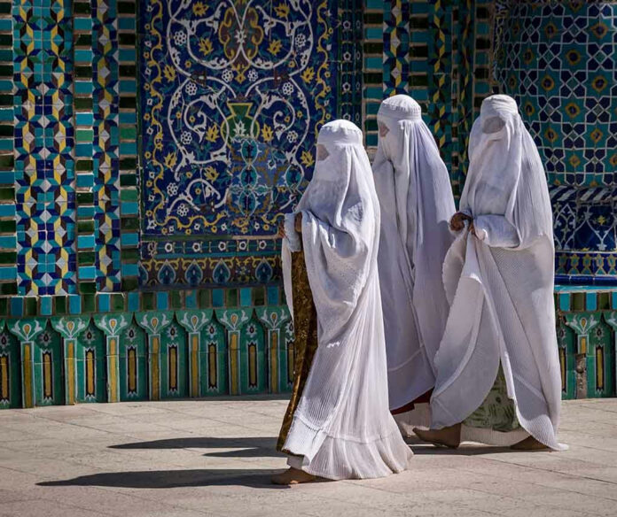 Three women in white traditional clothing, patterned wall background.
