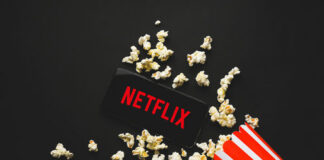 Spilled popcorn, phone displaying Netflix logo, striped popcorn container.