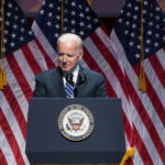 Jill Biden’s STROKE FEAR: What Was Hidden? Joe Biden speaking at podium with American flags behind.