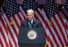 Jill Biden’s STROKE FEAR: What Was Hidden? Joe Biden speaking at podium with American flags behind.