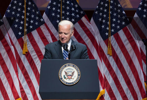 shutterstock_769773031 Joe Biden speaking at podium with American flags behind.