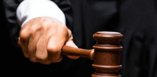 Judges hand gripping gavel on sounding block.