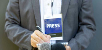 Press member holding microphones and taking notes.
