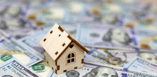 Mini house on top of hundred-dollar bills.