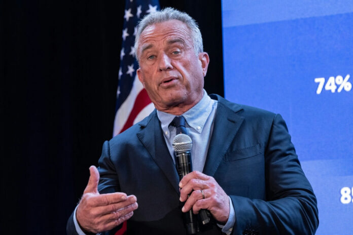 2456684697 A man in a suit speaking into a microphone at a political event with an American flag in the background