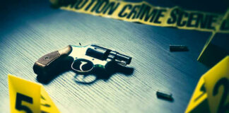 A revolver on a table surrounded by evidence markers and caution tape