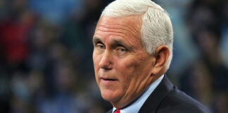 man with short white hair speaking at a podium
