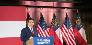 Man speaking at The Florida Blueprint event with flags.