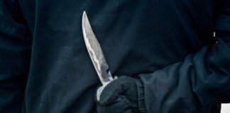 A gloved hand holding a knife behind the back