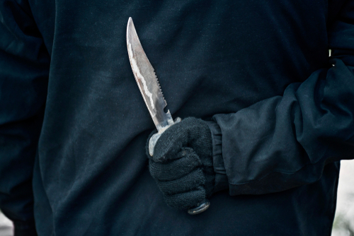A gloved hand holding a knife behind the back