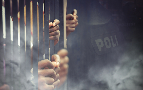 Hands gripping prison bars with a blurred police badge in the background