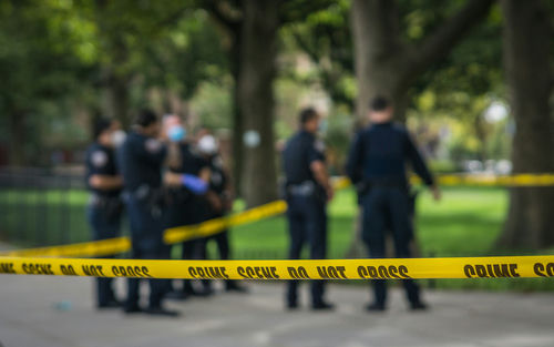 shutterstock_1814062073 Police officers behind yellow crime scene tape in park.