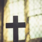 Wooden cross silhouette against a bright stained-glass window