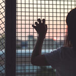 Person looking out through metal fence at sunset.