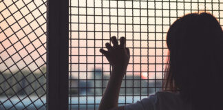 Person looking out through metal fence at sunset.