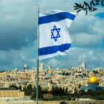 Israeli flag waving in front of the Jerusalem skyline with a golden dome in view