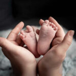 Mile 113 Miracle Stuns Jersey Hands holding newborn babys feet.