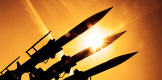 Silhouetted missiles on a launcher against a bright sunset sky
