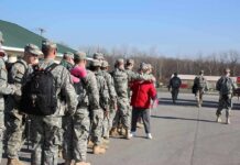 Soldiers in uniform line up outdoors with gear