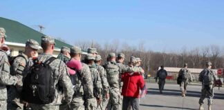 Soldiers in uniform line up outdoors with gear