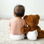 Luxury Parenting Team—Middle Class Gutted Baby in diaper sitting with teddy bear