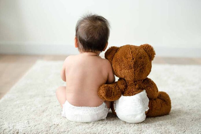 shutterstock_1273839757-1 Baby in diaper sitting with teddy bear
