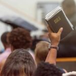 48% Shock: Politics Nukes Church Attendance? Hand holding a Bible in a crowded church service