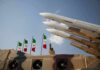 Airport Hit, Allies FUME — Tehran Miscalculated Missile launchers on a military vehicle with flags in the background