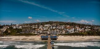 Aerial view of a pier extending into the ocean with a beach and residential area in the background