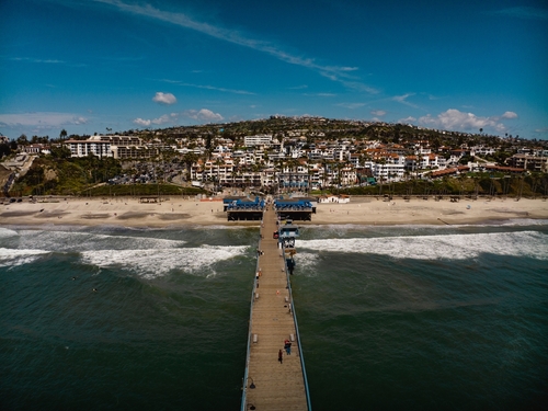 April,2024,,San,Clemente,,Ca,-,Drone,View,Of,San Aerial view of a pier extending into the ocean with a beach and residential area in the background