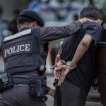 Police officer detains a handcuffed man beside a pickup truck