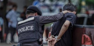 Police officer detains a handcuffed man beside a pickup truck