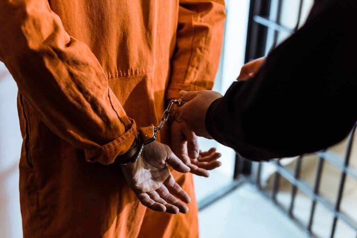 shutterstock_1036220185 Prisoner in orange jumpsuit handcuffed by officer
