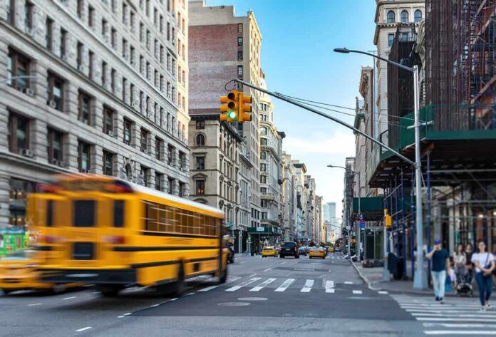 shutterstock_1148185430 City street with yellow school bus passing under traffic light