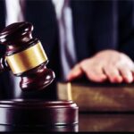 Judge's gavel striking block with hand on book in background
