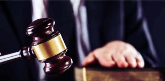 Judge's gavel striking block with hand on book in background