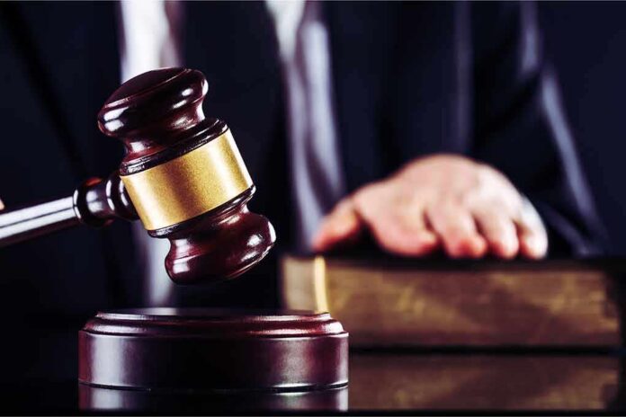 Judge's gavel striking block with hand on book in background