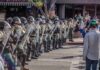 Riot police in helmets and shields form a line on a city street