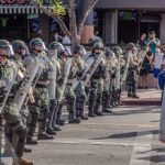 Riot police in helmets and shields form a line on a city street