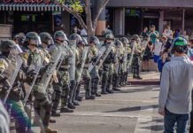 Riot police in helmets and shields form a line on a city street