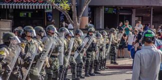 Riot police in helmets and shields form a line on a city street