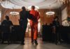 Sham Charity, Millions Vanish—Guess Where Prisoner in orange jumpsuit escorted by officer in a courtroom