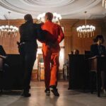 Sham Charity, Millions Vanish—Guess Where Prisoner in orange jumpsuit escorted by officer in a courtroom