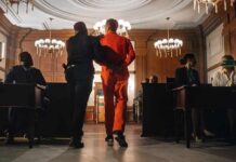 Sham Charity, Millions Vanish—Guess Where Prisoner in orange jumpsuit escorted by officer in a courtroom