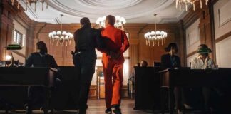 Prisoner in orange jumpsuit escorted by officer in a courtroom