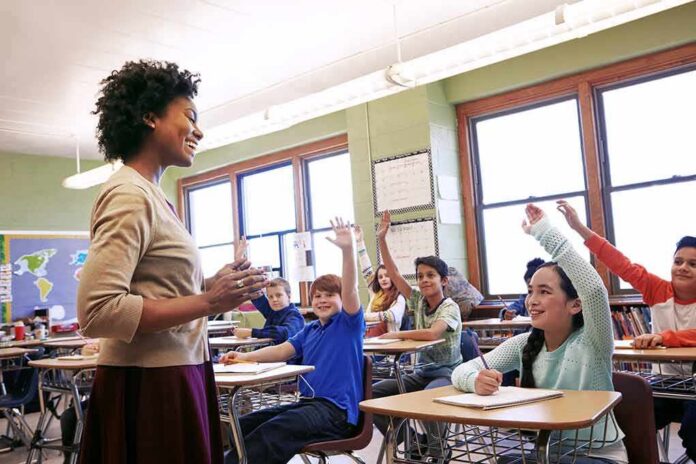 shutterstock_2250724177 Teacher engaging with students raising hands in a classroom