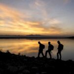 hikers silhouetted by a lake at sunset