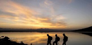 hikers silhouetted by a lake at sunset