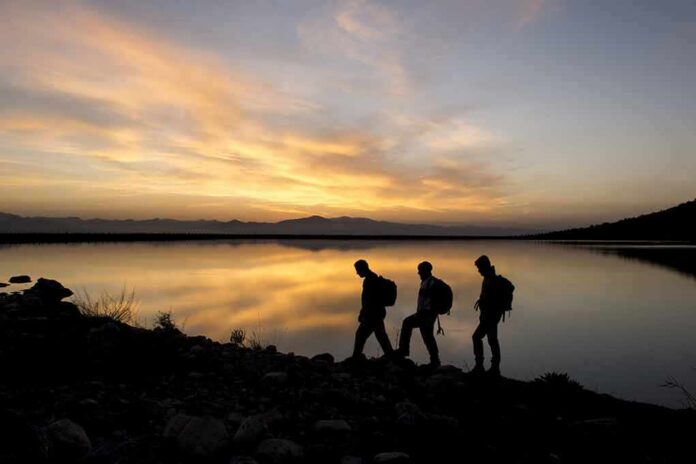shutterstock_270663746 hikers silhouetted by a lake at sunset